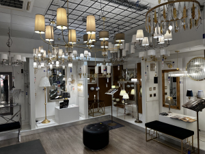 W tym fragmencie showroomu KOMA Oświetlenie Gdynia dominują klasyczne żyrandole z tekstylnymi abażurami w odcieniach beżu i bieli, eleganckie lampy stołowe oraz złote detale. 